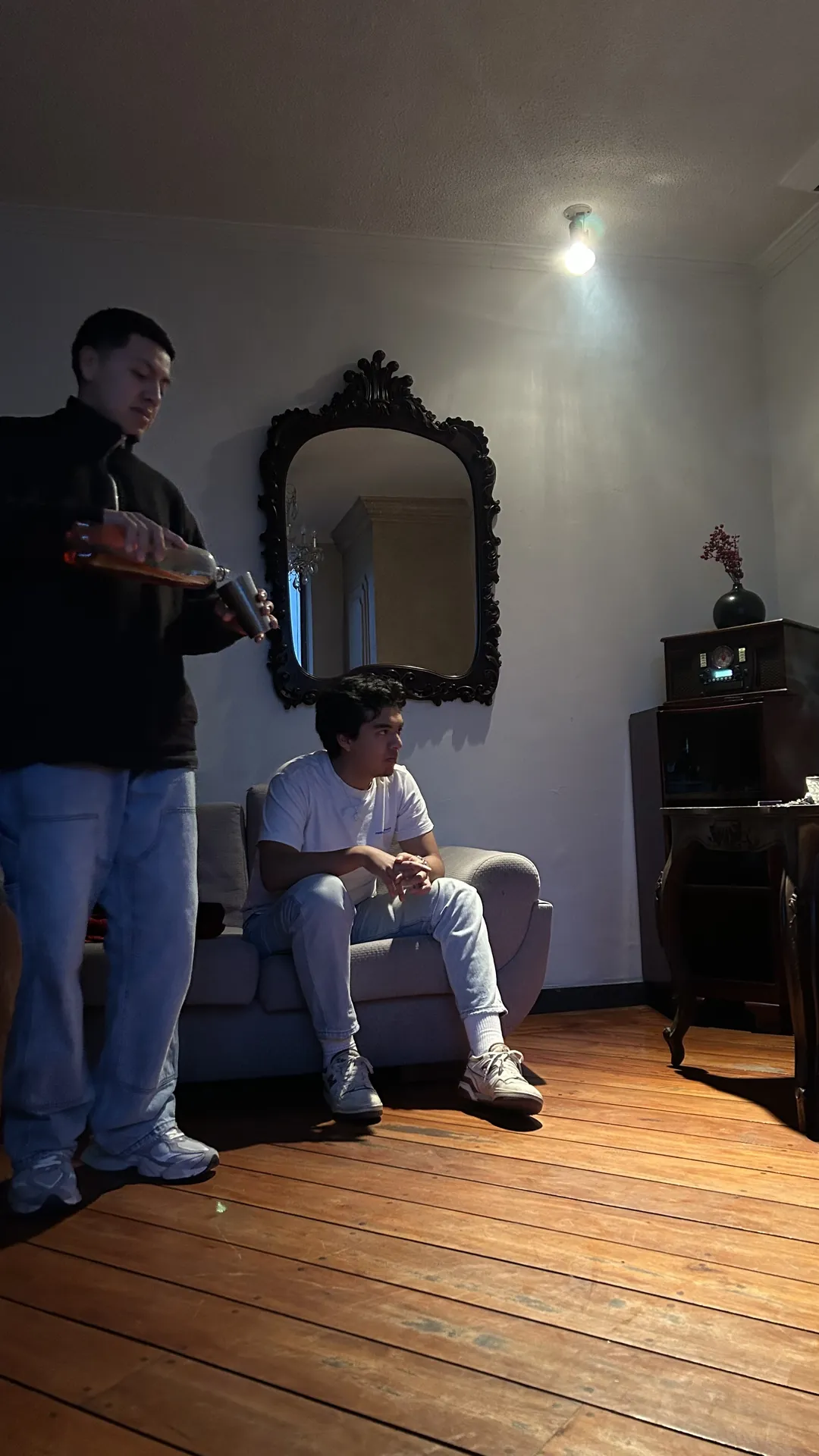Two friends in a wooden-floor room, both wearing light flare denim, full body.